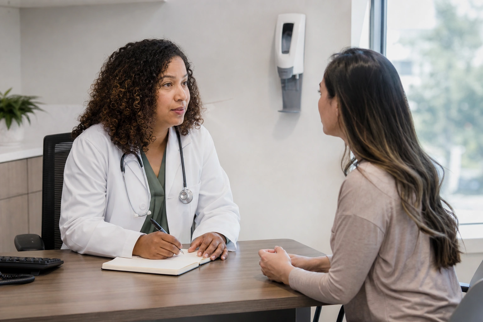 A primary-care clinician listening to an adult patient in a consultation room